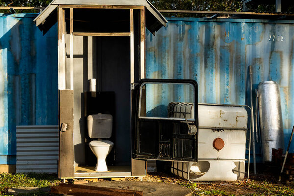 A unique backyard toilet with car door in early morning sunlight and shadows