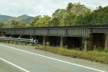 Kırsal bir otoyolun kenarındaki dereden geçen bir demiryolu köprüsü.