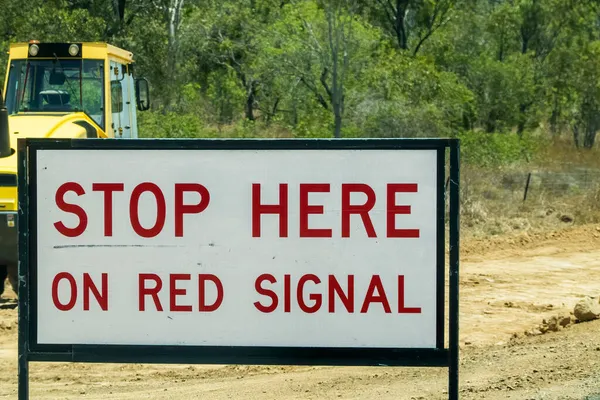 建設作業のための道路脇の標識背景に重い機械と赤の信号でここを停止するには ドライバーに警告 — ストック写真