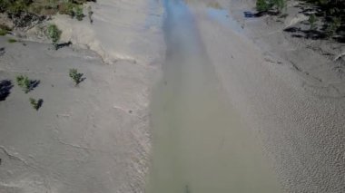 Çamurlu ve çamurlu bir derenin üzerinde insansız hava aracı uçuşu. Kıyılarda az miktarda su ve yerel bitki örtüsü var..