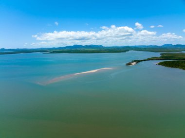 Deniz suyunun hava manzarası gelgit deresine akıyor. Etrafı tropikal bitki örtüsüyle çevrili. Bulutlu mavi bir gökyüzü ve dağ arkaplanı altında.