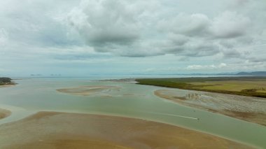 Bulutlu bir gökyüzünün altında okyanustan gelen alçak gelgitte nehir kanalında yelken açan iki küçük motorlu tekne.