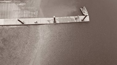 Rampanın yanında tekneyle bağlanmış, iskelede tanımlanamayan insanlar var. Monoton ve kontrastlı.