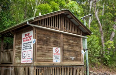 Conway Beach, Queensland, Avustralya - Aralık 2021: Cedar Creek Şelalesi 'nde ahşap klozet, insanları atlamamaları ve dalmamaları konusunda uyardı.