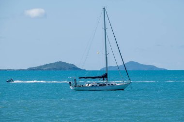 Airlie Beach, Queensland, Avustralya - Aralık 2021: Lüks bir yata güç veren bir jet ski adası ve dağ arkaplanıyla birlikte mavi gökyüzüne demirlemiş.