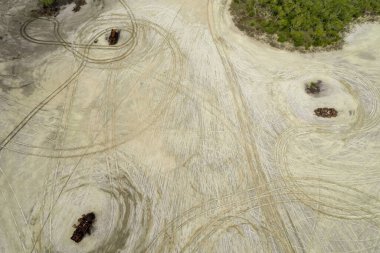 Kuru bir göl yatağında parçalanmaya bırakılmış paslı bir araba enkazı. Etrafında da araba ve motosiklet tekerleği izleri var. İnsansız hava aracı tepe görüntüsü.