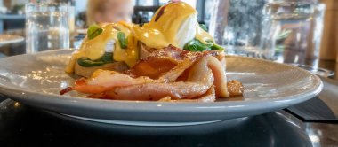 Tatil köyü restoranında tabakta Benedict usulü yumurta. Bulanık arkaplan yiyecekleri kapat.