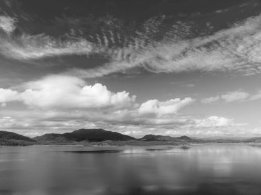 Bulut oluşumları suya yansıyan bir barajın durgun düz mavi suları. Güzel manzaralı drone hava manzarası.