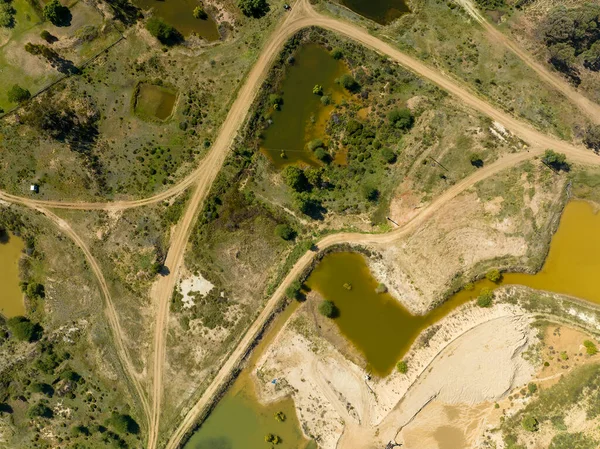 Drone aerial over ponds of water and dirt tracks caused by sapphire miners in central Queensland, Australia.