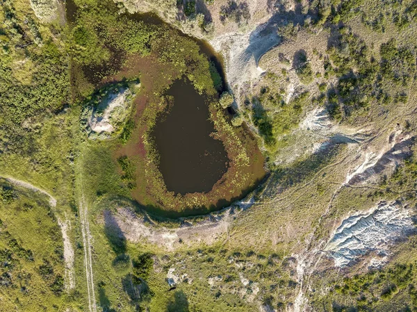 Looking down from drone onto a water pond edged with algae and a dirt track beside it. The Willows sapphire mine site Australia, abandoned.