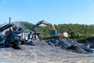 Mackay, Queensland, Australia - 7th June 2022: Machinery working in a quarry producing industrial rock and stone for construction of roads and other purposes.