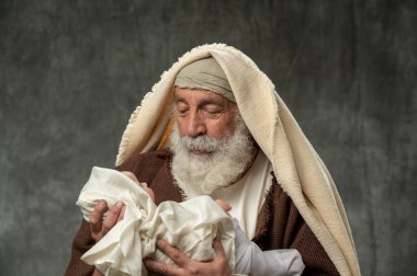 Simeon, bebek İsa 'yı dar gri arka planda tutuyor.