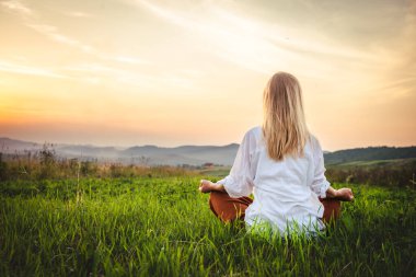 Dağın tepesindeki yeşil çimlerde yoga yapan kadın gün batımında güzel manzaralı.