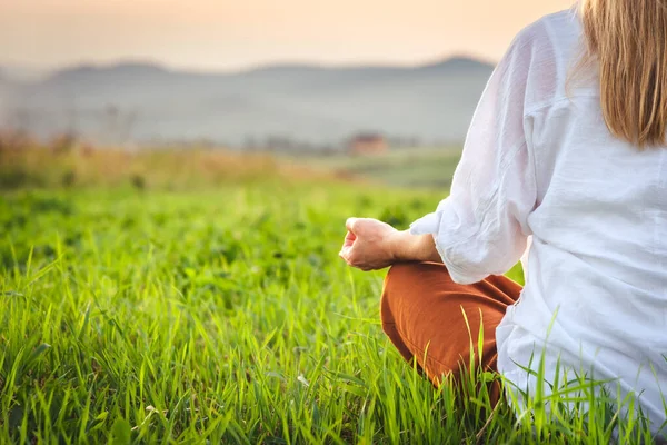 Dağın tepesindeki yeşil çimlerde yoga yapan kadın gün batımında güzel manzaralı.