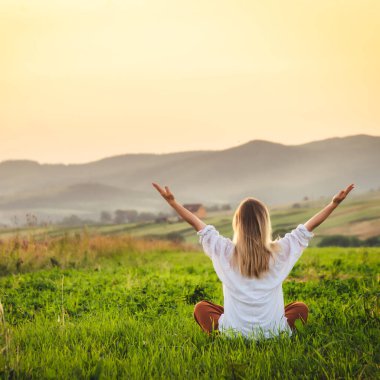 Dağın tepesindeki yeşil çimlerde yoga yapan kadın gün batımında güzel manzaralı.