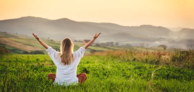 Dağın tepesindeki yeşil çimlerde yoga yapan kadın gün batımında güzel manzaralı.