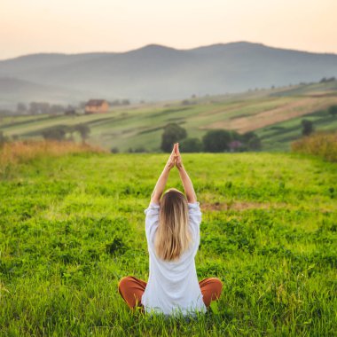 Woman doing yoga on the green grass on the top of the mountain with beautiful view at sunset