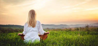 Dağın tepesindeki yeşil çimlerde yoga yapan kadın gün batımında güzel manzaralı.