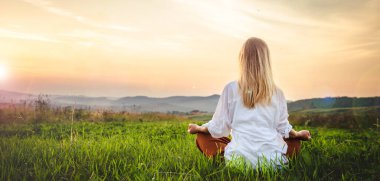 Dağın tepesindeki yeşil çimlerde yoga yapan kadın gün batımında güzel manzaralı.