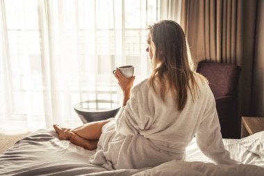 Young woman with bathrobe have a Breakfast in bed, cozy hotel room.