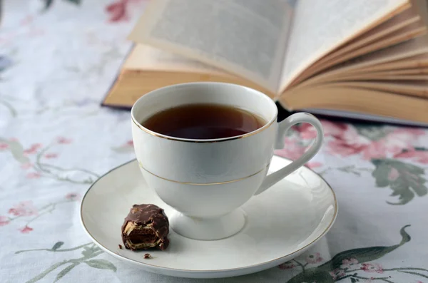 Taza blanca de té con dulces cerca del libro — Foto de Stock