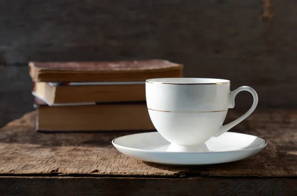 Copa blanca sobre una mesa de madera con libros — Foto de Stock