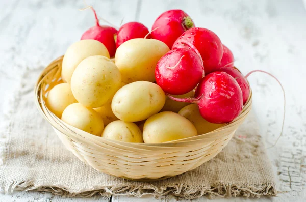 Fresh young potatoes and radishes in a basket — Stock Photo, Image