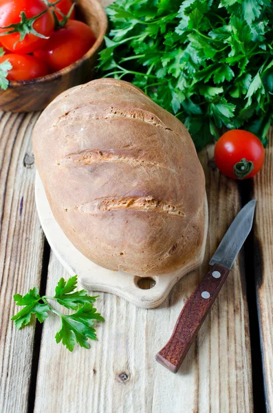 Hembakat bröd på träbord med färska grönsaker — Stockfoto