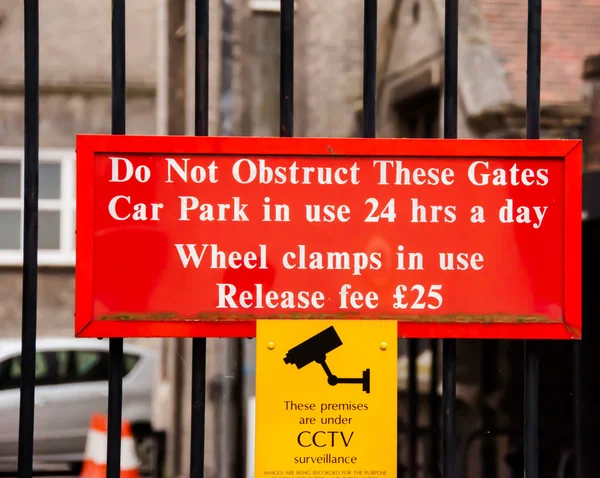 Warning sign for motorists Do not obstruct these gates, car park in use 24 hours a day, wheel clamps in use — Stock Photo, Image