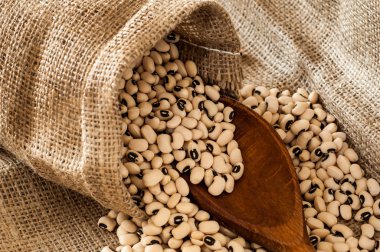 Black eyed peas in jute bag spilled on jute background with wood
