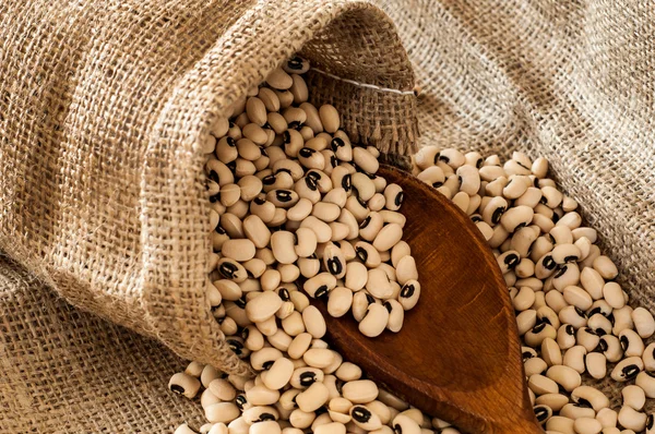 Black eyed peas in jute bag spilled on jute background with wood — Stock Photo, Image