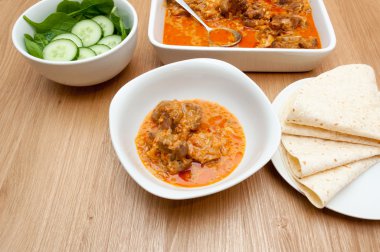 Indian curry lamb rogan josh in a white dish, with naan bread. clipart