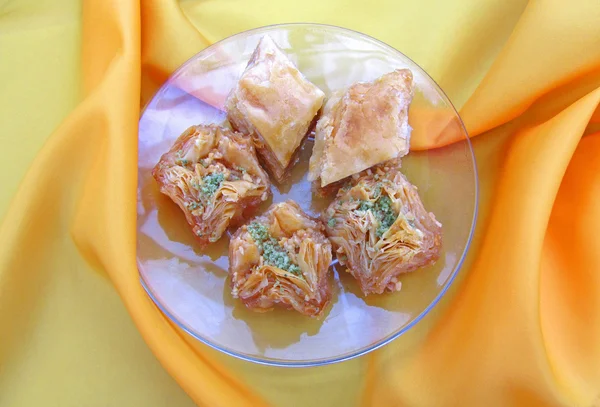 Sweet baklava on saucer on orange tablecloth, close-up — Stock Photo, Image