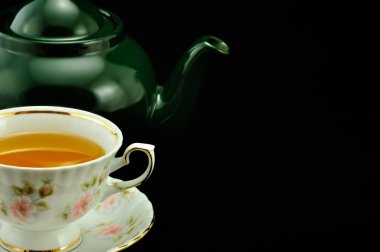 Porselen çay bardağı çay ve yeşil çaydanlık üstünde siyah bir backgr dolu