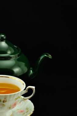 Porselen çay bardağı çay ve yeşil çaydanlık üstünde siyah bir backgr dolu