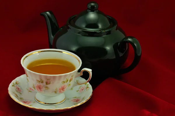 Een kopje thee en groene theepot op een rode achtergrond — Stockfoto