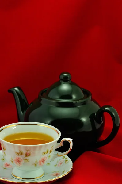 Une tasse de thé et une théière verte sur fond rouge — Photo