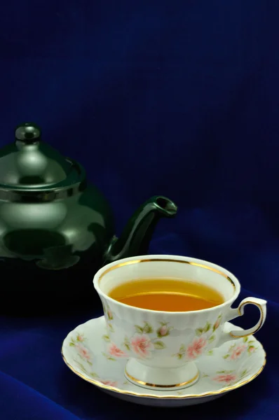 Une tasse de thé et une théière verte sur fond bleu — Photo