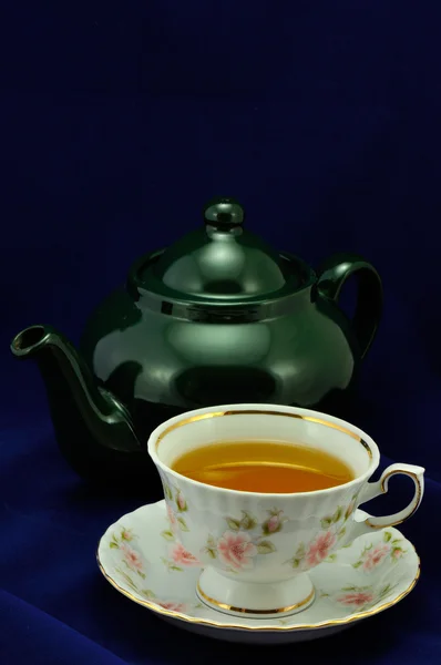Uma xícara de chá e bule verde em um fundo azul — Fotografia de Stock
