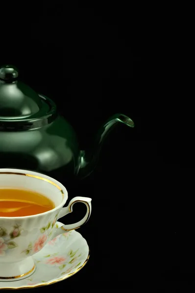 Porcelain tea cup full of tea and green teapot on a black backgr — Stock Photo, Image