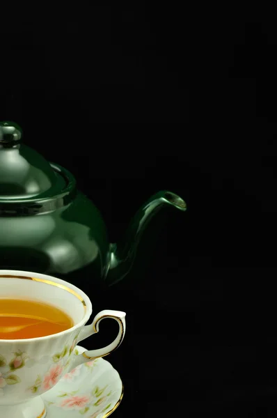 Porcelain tea cup full of tea and green teapot on a black backgr — Stock Photo, Image