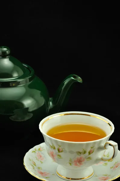 Porcelain tea cup full of tea and green teapot on a black backgr — Stock Photo, Image