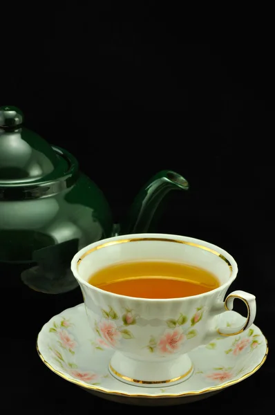 Porcelain tea cup full of tea and green teapot on a black backgr Royalty Free Stock Images