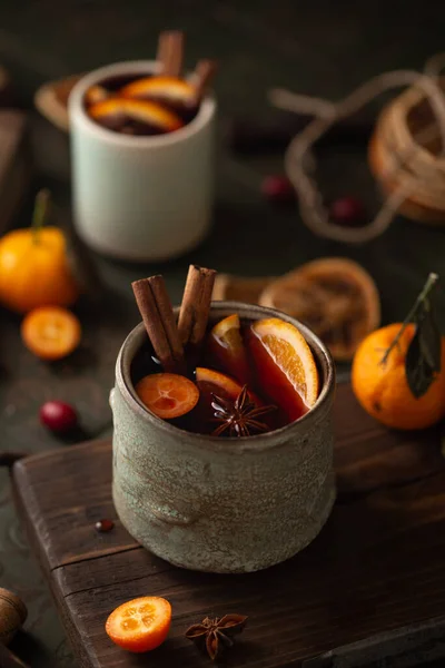 Zbliżenie grzanego wina w ceramicznym kubku z pomarańczami, mandarynkami, paluszkami cynamonowymi, gwiazdami anyżu i goździkami na drewnianej desce. — Zdjęcie stockowe