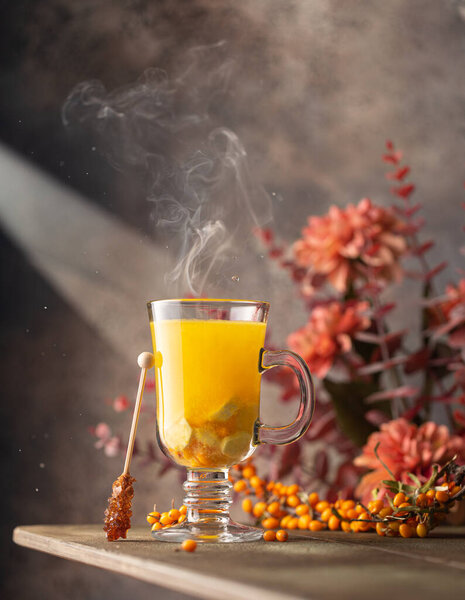 Sea buckthorn tea in a glass with fresh berries,smoke and autumn flowers on background.Close up of healthy hot drink.