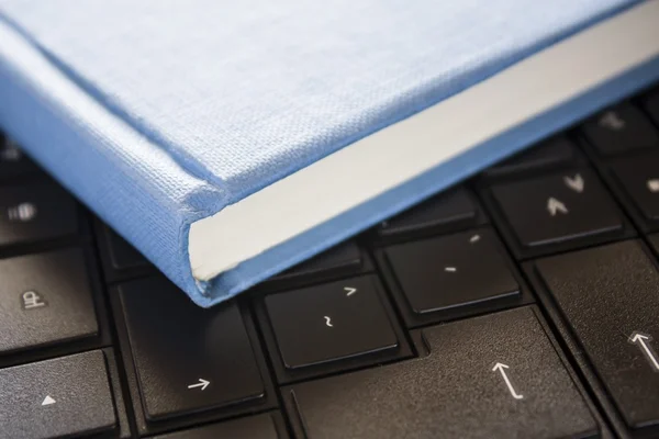 Livro azul sobre computador preto com luz de janela — Fotografia de Stock