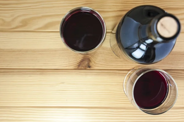 Red wine glasses and bottle over pine wood table — Stock Photo, Image