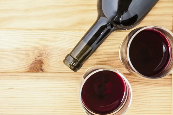 Red wine glasses and bottle over pine wood table — Stock Photo, Image