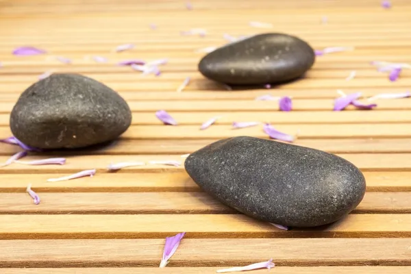 Zen stones with petals on slatted wood background — Stock Photo, Image