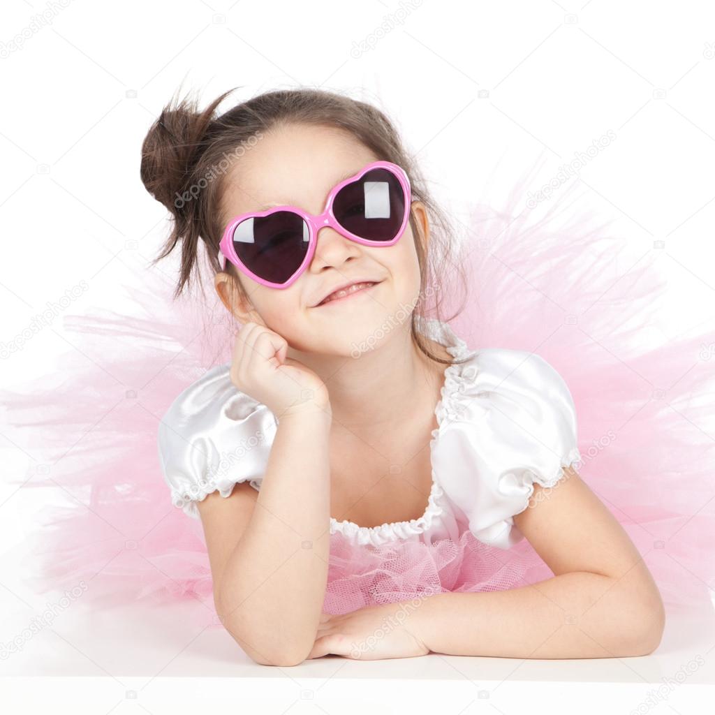 Beautiful little girl with glasses in a pink dress over white